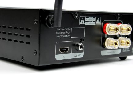Sort metalhus i rektangulær form, bagside i tæt op, med perforerede ventilationshuller, drejbar antenne, HDMI-port, koaksialudgang og fire gyldne højttalerterminaler
