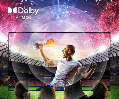 Televisor grande con marco negro de plástico de bordes finos, vista frontal, mostrando en pantalla una escena de fútbol con un jugador alzando un trofeo en medio de un estadio iluminado por fuegos artificiales y rodeado de círculos translúcidos que evocan ondas sonoras.