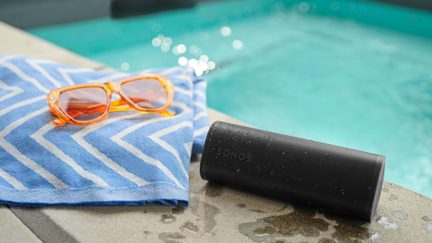 Speaker Bluetooth Sonos nera sul bordo di una piscina, vicino a un asciugamano blu e a occhiali arancioni