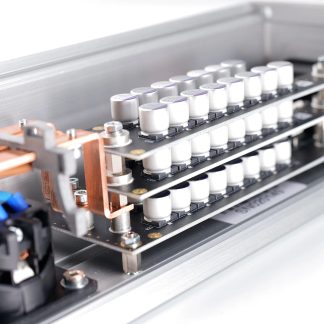 Zblízka zobrazený pohled na elektronický modul s hliníkovým stříbrným pouzdrem, sběrnicemi z mědi a řadami malých válcových bílých kondenzátorů