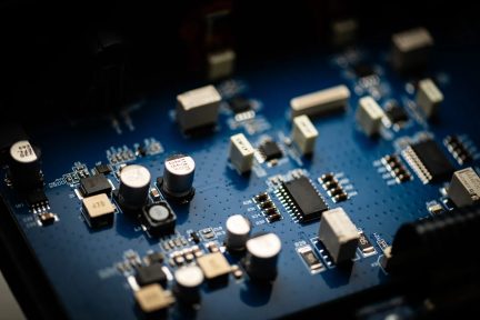 Niebieska płytka elektroniczna w zbliżeniu z układami scalonymi i kondensatorami, widok pod kątem na zmontowaną płytkę drukowaną