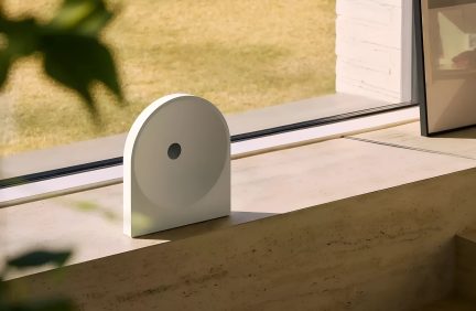 Luce notturna di design bianca a forma di arco con cerchio centrale e piccolo pulsante nero appoggiata su un davanzale della finestra