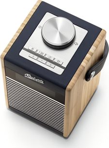 Roberts Rambler Midi bordradio i mørkeblå farve, kubisk trækasse i lys træ med metalgitterfront og diskret display, top belagt med mørkeblåt kunstlæder udstyret med en stor central metaldrejeknap og skjulte knapper, synligt sidehåndtag, trekvart faldende perspektiv
