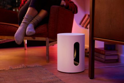 Hvid Sonos Sub Mini-subwoofer på gulvet ved siden af en lænestol i en rosa oplyst stue