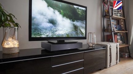 Fladskærms-TV, der viser en boblende vandfald, placeret på et mørkt træmøbel med et lydsystem og dekorationer