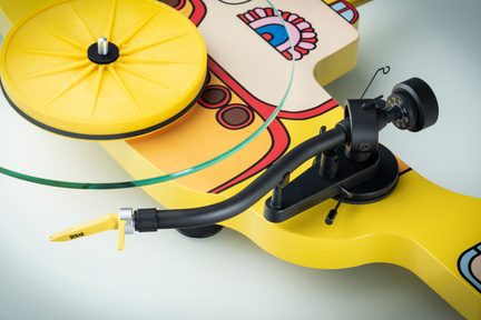 Yellow circular turntable with a central axis, curved black tonearm, yellow stylus, and a base adorned with colorful patterns.