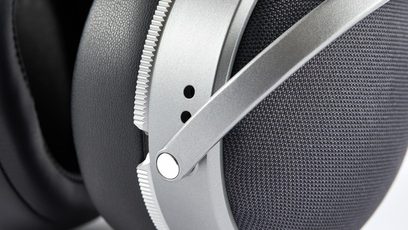 Seitliche Nahaufnahme der Ohrmuschel des geschlossenen, kabelgebundenen HiFi-Kopfhörers Audeze LCD-S20 aus silberfarbenem Metall mit gezacktem Ring, Außenschale aus dunkelgrauem Mesh-Gewebe und großem schwarzen Kunstleder-Polster.