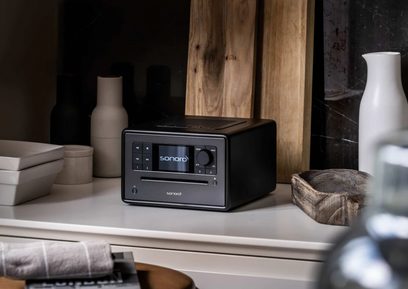 Λαμπερό μαύρο-ασημί ραδιόφωνο Sonoro Elite - μπροστινή όψη, τοποθετημένο σε ξύλινο ράφι με διακοσμητικά αντικείμενα