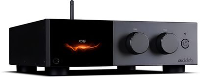 Tredjehandsvy snett framifrån vänster av Audiolab D9 DAC-ljudomvandlare, rektangulärt svart metallchassi på fötter, frontpanel uppdelad mellan en glänsande orangebelyst display till vänster som visar D9 och, till höger, två stora rattar samt strömknapp, vertikal antenn baktill