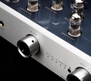 Nærbillede fra venstre forhjørne af Cayin CS-55A EL34 integreret stereo rørforstærker, frontpanel i børstet sølvfarvet aluminium med stor metalvolumenkontrol, øverste kabinet i metallisk blå med fire synlige vakuumrør