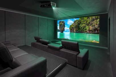 Optoma UHZ65 videoprojektor, der projicerer et billede af et tropisk landskab på en stor skærm i et mørkt rum med grå sofaer