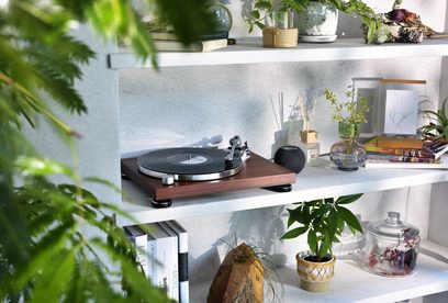 Giradischi in legno Audio Technica AT-LPW50BTRW su mensola bianca con piante, libri, diffusore e oggetti decorativi