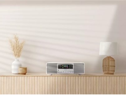 Sonoro Primus glossy white - silver radio on light wood shelf with white vase, white lamp, and dried plant