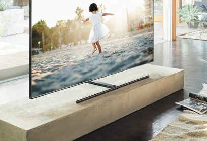 Televizor Samsung QE65Q9F 2018 zobrazující obrázek malé dívky v bílé šatičce skákající na pláži při západu slunce