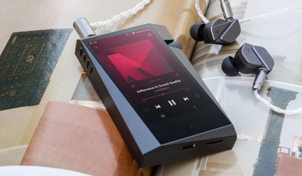 Black portable audio player with screen displaying "Difference in Sound Quality", wireless headphones and earbuds on open book