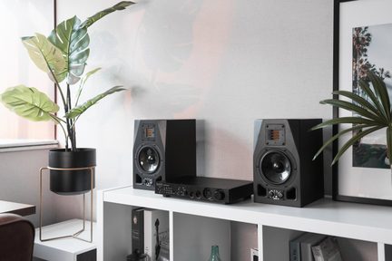 Schwarze Hi‑Fi-Regal-Lautsprecher mit Audioverstärker auf weißem Regal, minimalistisches Dekor mit grünen Pflanzen
