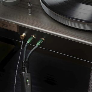 Phono-kabel Black Hole GroundGoody 3m med grønne metalstik, sort flettet kappe, tilsluttet en pladespiller på træoverflade