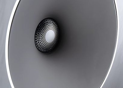 Altoparlante circolare nero visto frontalmente in un cabinet ovale grigio scuro, illuminazione laterale che crea un riflesso bianco