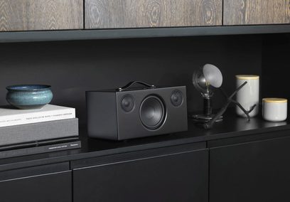 Audio Pro ADDON C10 sort højttaler, set forfra, med højttalere, knapper og stik på et mørkt trækabinet