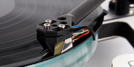 Close-up of a turntable, black tonearm, cartridge with red, green, blue cables, black record, shiny surface, diagonal angle