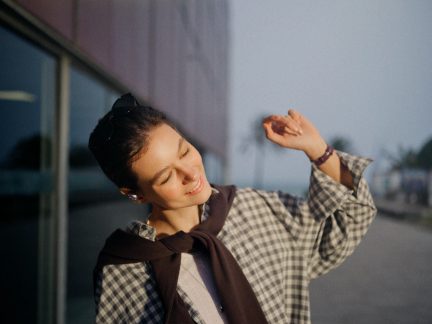 Camicia a quadri beige e marrone indossata con maglione marrone annodato sulle spalle e occhiali da sole neri