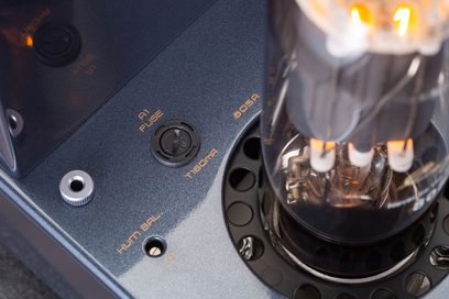 Detailní pohled shora na stereofonní lampařský integrovaný zesilovač Cayin Jazz 100 v černé barvě, tmavý kovový rám s oranžovými nápisy, rozžhavená lampa 805A a pojistkový držák A1