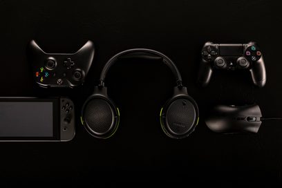 Audeze Penrose Xbox gaming headset i sort, set forfra, og sorte Xbox Series-controllere, set forfra og bagfra, på sort baggrund