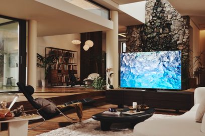 Moderne stue med sofa, lænestol, sofabord, bogreol, stenbrændeovn og stor Samsung QE75QN900B-tv, der viser et blåt abstrakt billede