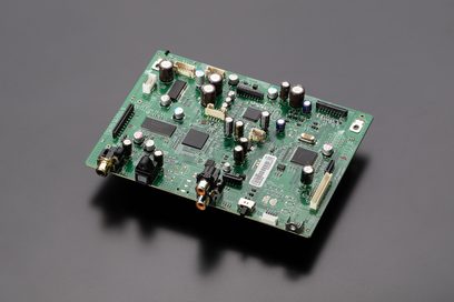 Rectangular green circuit board with numerous metallic and plastic electronic components of various sizes and shapes