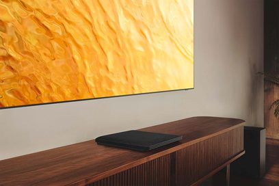 Samsung QE75QN800B 2022 fladskærms-tv stillet på træmøbel, skærmen viser orange-gult abstrakt mønster, sort fjernbetjening foran
