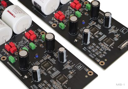 Scheda elettronica Matrix Audio MS‑1 PRE nera in resina epossidica, vista a tre quarti dall’alto, con chip AKM, condensatori elettrolitici cilindrici neri con parte superiore argentata, grandi condensatori a film cilindrici bianchi e piccoli moduli plastici rossi e verdi