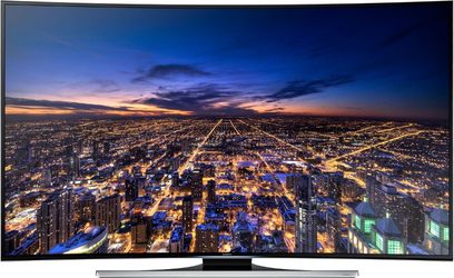 Samsung UE55HU8200 TV viser et natteluftsyn over en oplyst by med tætpakkede bygninger og gittermønstrede gader