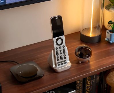 Ahşap mobilya üzerinde şarj istasyonlu gümüş renkli evrensel uzaktan kumanda, siyah hub ve küçük küresel cihaz