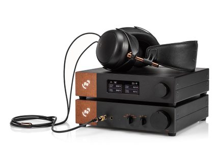Amplificador de audio negro con dos auriculares negros conectados, visto de frente sobre fondo blanco