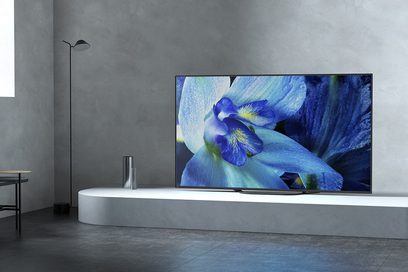 Sony KD-55AG8 fladskærms-TV, der viser en blå iris-blomst på sort baggrund, set forfra, stående på et hvidt møbel