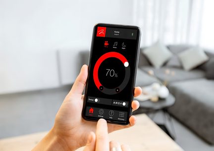 Chytrý telefon v černé barvě s dotykovým displejem zobrazujícím červeno-černé kruhové ovládací rozhraní, držený v ruce