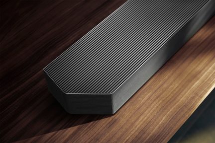 Schwarze Soundbar aus Metall mit gerippter Oberseite und Samsung-Logo, seitlich mit gelochtem Gitter verkleidet, aus schräger Vogelperspektive aufgenommen