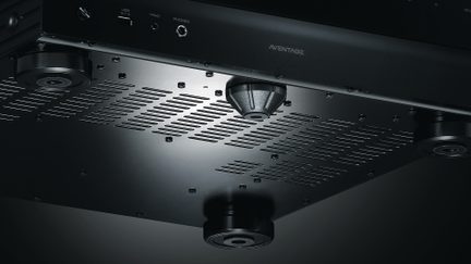 Low-angle view of a black device with ventilation grilles, 4 circular feet, and a central conical foot marked Aventage