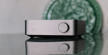 Custodia rettangolare argentata con un pulsante circolare a destra, tre indicatori luminosi e un pulsante a sinistra, superficie riflettente