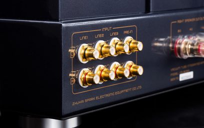 Primer plano en ligero ángulo trasero derecho de ocho conectores RCA dorados con aislante blanco, rodeados de serigrafías doradas, montados sobre la carcasa metálica negra del amplificador integrado estéreo a válvulas Cayin CS-805A