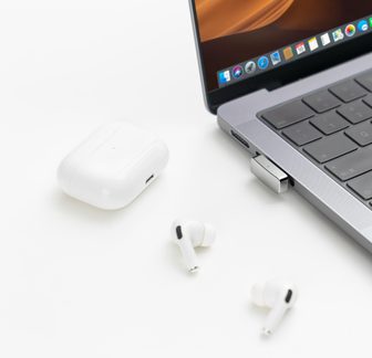 Auricolari wireless bianchi tipo AirPods Pro con custodia e dongle USB su MacBook grigio su sfondo bianco