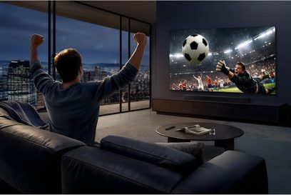 Televisore Samsung TMR65R95H grande schermo a parete in un soggiorno moderno, partita di calcio vista di spalle da uno spettatore
