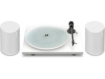 Vit vinylskivspelare med genomskinlig tallrik och två vita Sonos-högtalare på vardera sidan