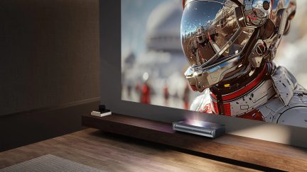 Room with laser projector on wooden shelf, astronaut image projected on wall, wooden floor, gray rug