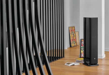 Casse nere verticali, quadro astratto colorato, libri impilati, taccuino giallo su un pavimento in legno chiaro davanti a una parete bianca