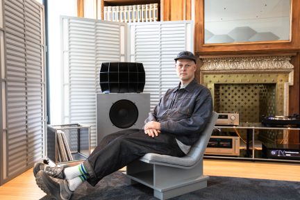 Man zittend op grijze fauteuil voor hi-fi-luidspreker en platenspeler in een luisterruimte