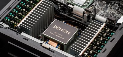 Indvendigt billede af en sort Denon AVC-X8500H-forstærker, der viser de elektroniske komponenter, køleribber og transformeren