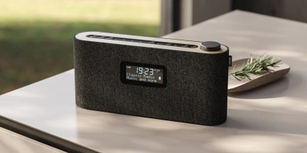 Radio sveglia Bluetooth Loewe grigio scuro con schermo centrale, pulsanti sulla parte superiore e manopola laterale su un tavolo