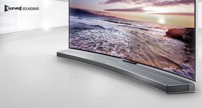 Zakřivený soundbar Samsung HW-H7501 pod televizí zobrazující pláž při západu slunce, pohled zepředu