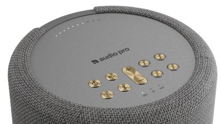Harmaa ja sylinterinmuotoinen langaton Audio Pro -kaiutin, jossa on punottu verhoilu ja kullanväriset painikkeet päällä